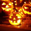 Drei leuchtende Halloween-Kürbisse mit geschnitzten Gesichtern in unterschiedlicher Größe, unscharfer Hintergrund mit Lichterketten