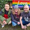 drei Personen vor einer Regenbogenflagge